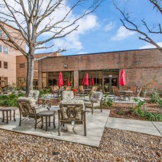 A cozy outdoor patio area with comfortable seating and red umbrellas, set against a brick building.