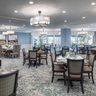A spacious dining room with elegant decor, featuring multiple tables and chairs, chandeliers, and a carpeted floor.