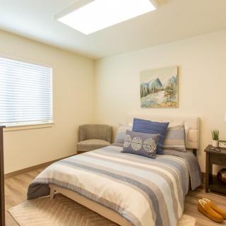 A cozy bedroom interior with a neatly made bed, artwork on the wall, and soft natural lighting.