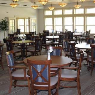 An empty dining room with wooden tables and chairs, large windows, and ceiling fans.