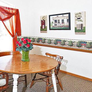 A cozy dining room with a wooden table and chairs, decorated with wall art and red flowers in a vase.