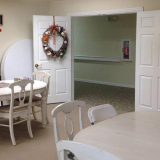 A cozy dining area with white tables and chairs, featuring a decorative wreath on the open door.