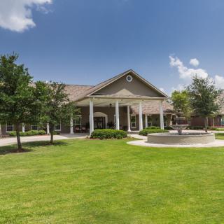 A spacious building with a well-maintained lawn and surrounding trees under a clear blue sky.