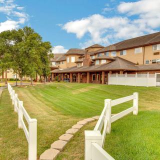 A scenic view of a building with a manicured lawn, white fence, and pathway under a partly cloudy sky.