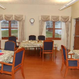 A cozy dining area with tables and chairs arranged neatly, featuring large windows with curtains.