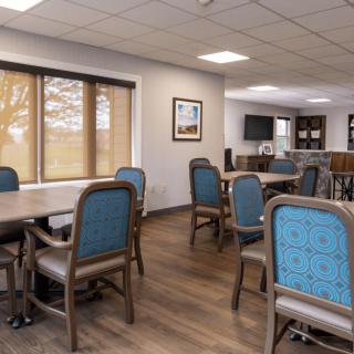 A spacious dining room with tables and chairs, featuring large windows and a wooden floor.