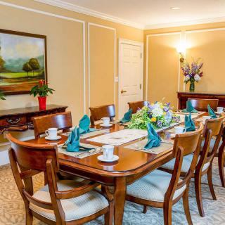 An elegantly set dining room with a large table and chairs, adorned with teal napkins, cups, and floral centerpieces.