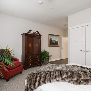 A cozy bedroom featuring a large wooden wardrobe, a red armchair, and a fur throw on the bed.