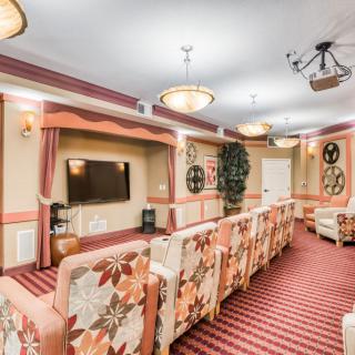 A cozy theater room with floral-patterned seating, a television mounted on the wall, and soft decorative lighting.