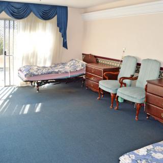 A spacious bedroom with sunlight streaming through the window, featuring a bed, multiple chairs, and elegant drapes.