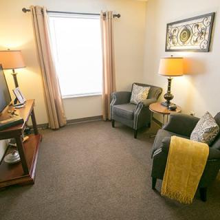 A cozy living room with armchairs, lamps, and decorative art on the wall.