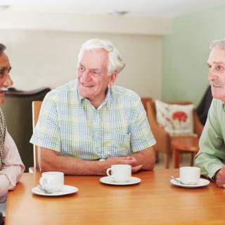 Three elderly men enjoying a conversation over coffee at a table.