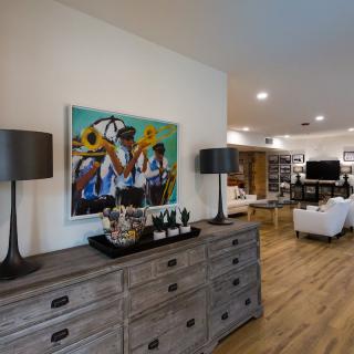 A modern living room with a wooden dresser, decorative lamps, and a colorful artwork on the wall.