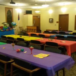 A brightly decorated indoor party setup with colorful tablecloths and balloons.