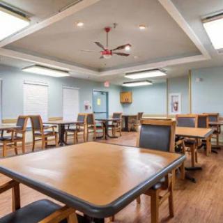 A spacious and well-lit dining area featuring simple wooden tables and comfortable chairs, ready for gatherings.