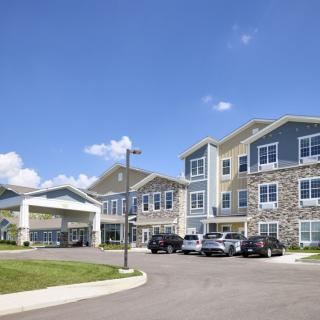 A modern residential building with a parking lot and cars under a clear blue sky.