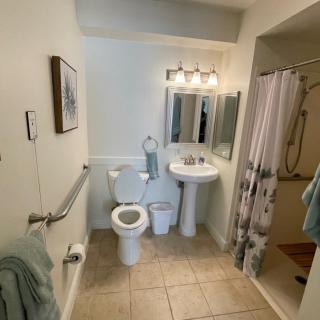 A clean and accessible bathroom with a toilet, sink, mirror, and shower.