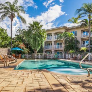 A tropical resort with a swimming pool surrounded by palm trees under a clear blue sky.