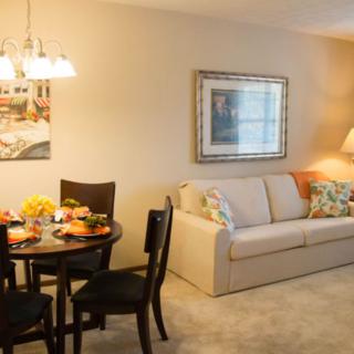 A cozy living and dining area featuring a comfortable sofa, round dining table set for a meal, decorative artwork, and warm lighting.