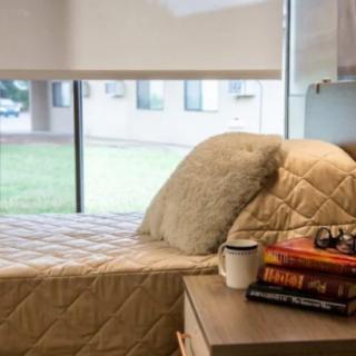 A cozy bedroom setup with a neatly made bed, fluffy pillows, and a stack of books beside a mug on the nightstand with natural light streaming through the window.