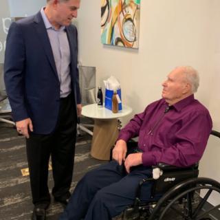 A man is engaging in a conversation with an elderly person seated in a wheelchair indoors.