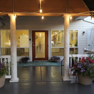 A warmly lit house entrance with a porch and decorative plants.