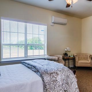 A cozy bedroom with a bed, comfortable seating, and a large window letting in natural light.