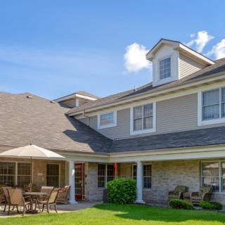 A sunny day view of a spacious two-story house with a well-maintained lawn and patio furniture.