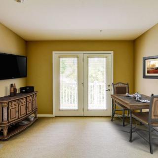 A cozy living room with a table and chairs, television mounted on the wall, and double doors leading outside.