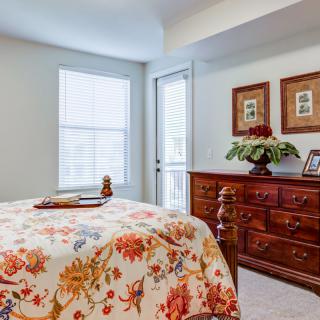 A cozy bedroom featuring floral bedding and a wooden dresser with decorative frames and a plant.