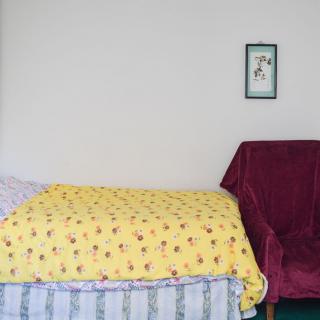 A minimalist bedroom with a bed covered by a yellow blanket and a burgundy chair.