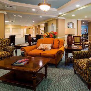 A cozy living room featuring a vibrant orange sofa surrounded by patterned armchairs, centered around a wooden coffee table in a warmly lit space.