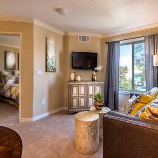 A cozy living room with modern decor, featuring a wall-mounted TV and large windows.
