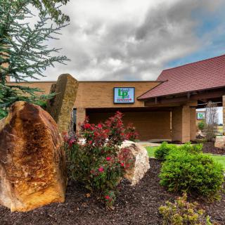 Exterior view of a hotel entrance with landscaping under a cloudy sky.
