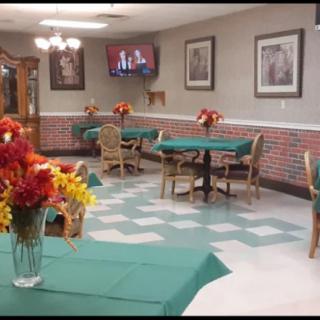 A cozy dining area with green tablecloths, decorated with floral centerpieces, and a television mounted on the wall.