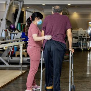A healthcare professional assists an elderly patient during a rehabilitation session.