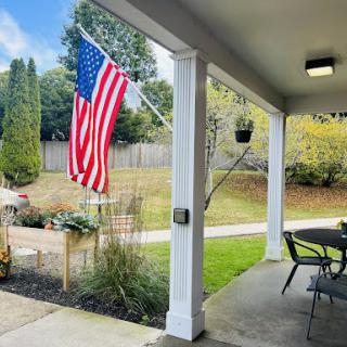 A peaceful outdoor setting featuring an American flag on the porch, surrounded by greenery and a well-maintained garden.