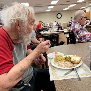 An elderly man enjoying his meal in a communal dining setting.