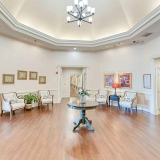 A spacious lobby area with elegant decor, featuring a central round table, comfortable chairs, and a large chandelier.