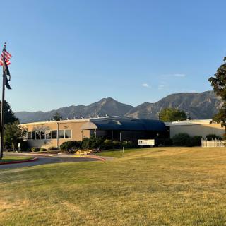 A clear day showcasing a building with mountains in the background, accompanied by an American flag and a grassy area.