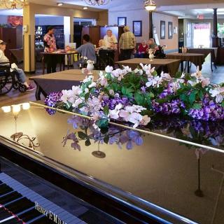 A cozy restaurant scene featuring a piano adorned with vibrant flowers, with patrons dining in the background.