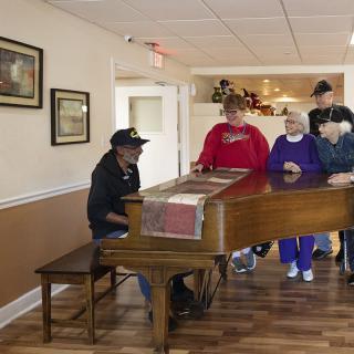 A group of people gathered around a piano to enjoy a musical performance indoors.