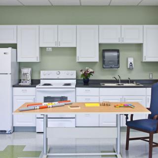 A clean, modern kitchen with white cabinets and appliances, featuring a table and chair in the foreground.