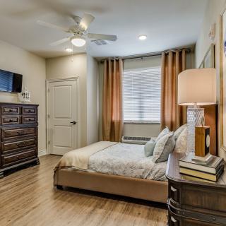 A cozy bedroom with a neatly made bed, a dresser, and warm lighting.