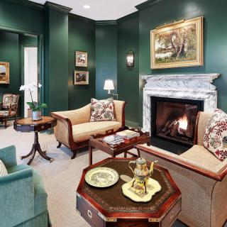 A cozy living room with green walls, traditional furniture, and a marble fireplace.