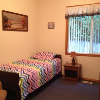 A cozy bedroom with a single bed featuring colorful zigzag bedding, a nightstand, and wall art.