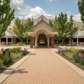 A pathway leads to an elegant building surrounded by landscaped gardens and trees on a sunny day.