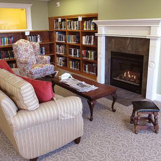 A cozy library corner featuring a sofa, armchair, coffee table, and a warm fireplace surrounded by bookshelves.