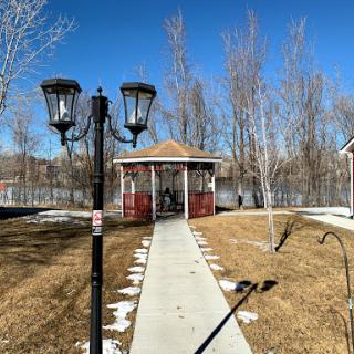A serene view of a gazebo surrounded by trees, with a clear blue sky and a pathway leading to it.