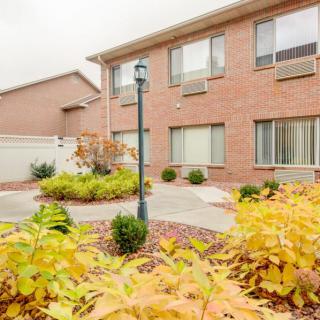A residential brick building with a landscaped courtyard featuring autumn foliage and a lamp post.